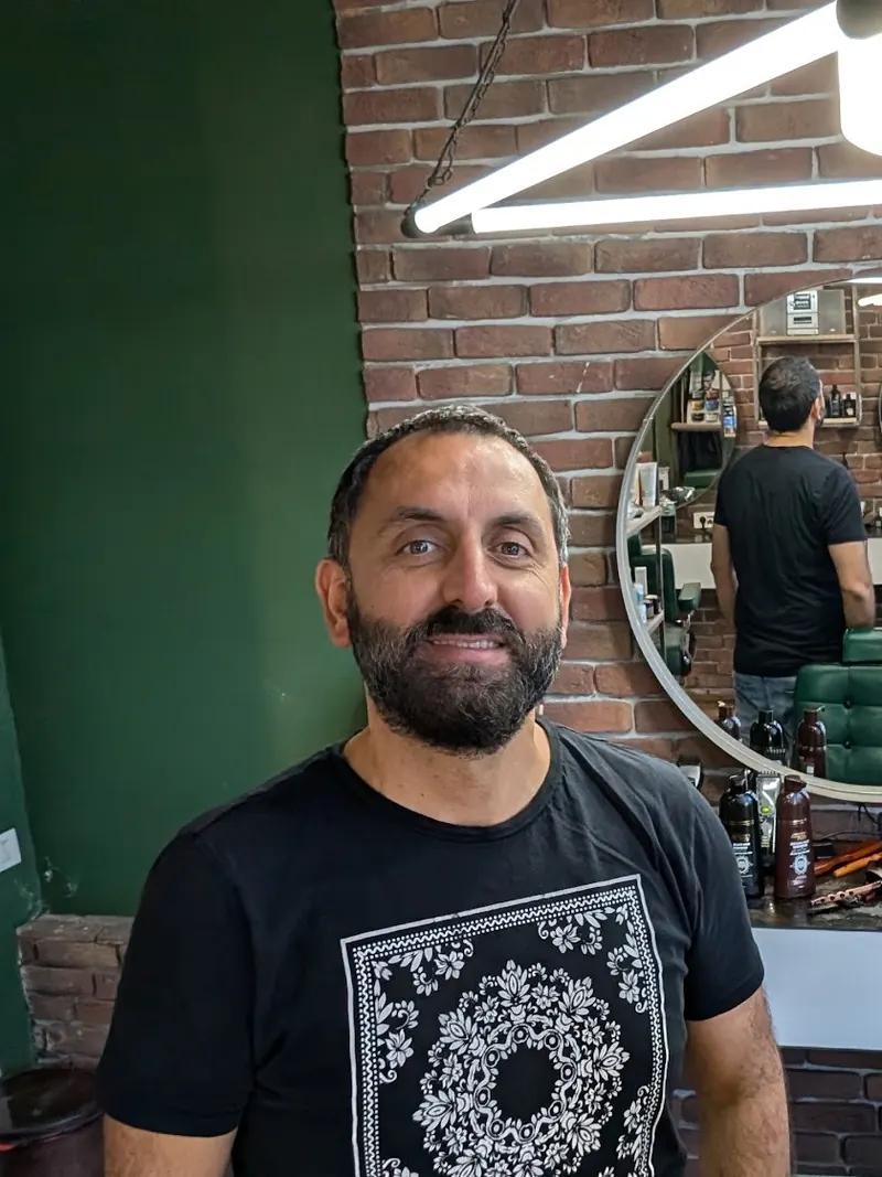 Portrait of the barber in the shop, brick wall and round mirror behind him