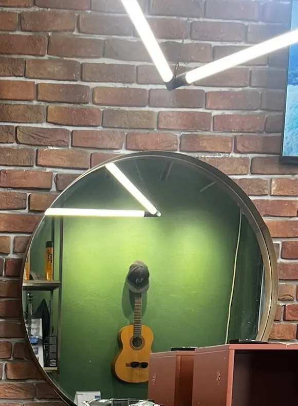 A round mirror reflecting the green wall and a guitar