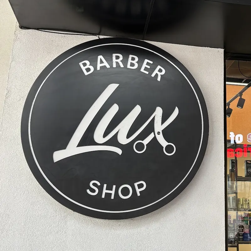 The round black LUX Barber Shop sign on the white wall outside the shop
