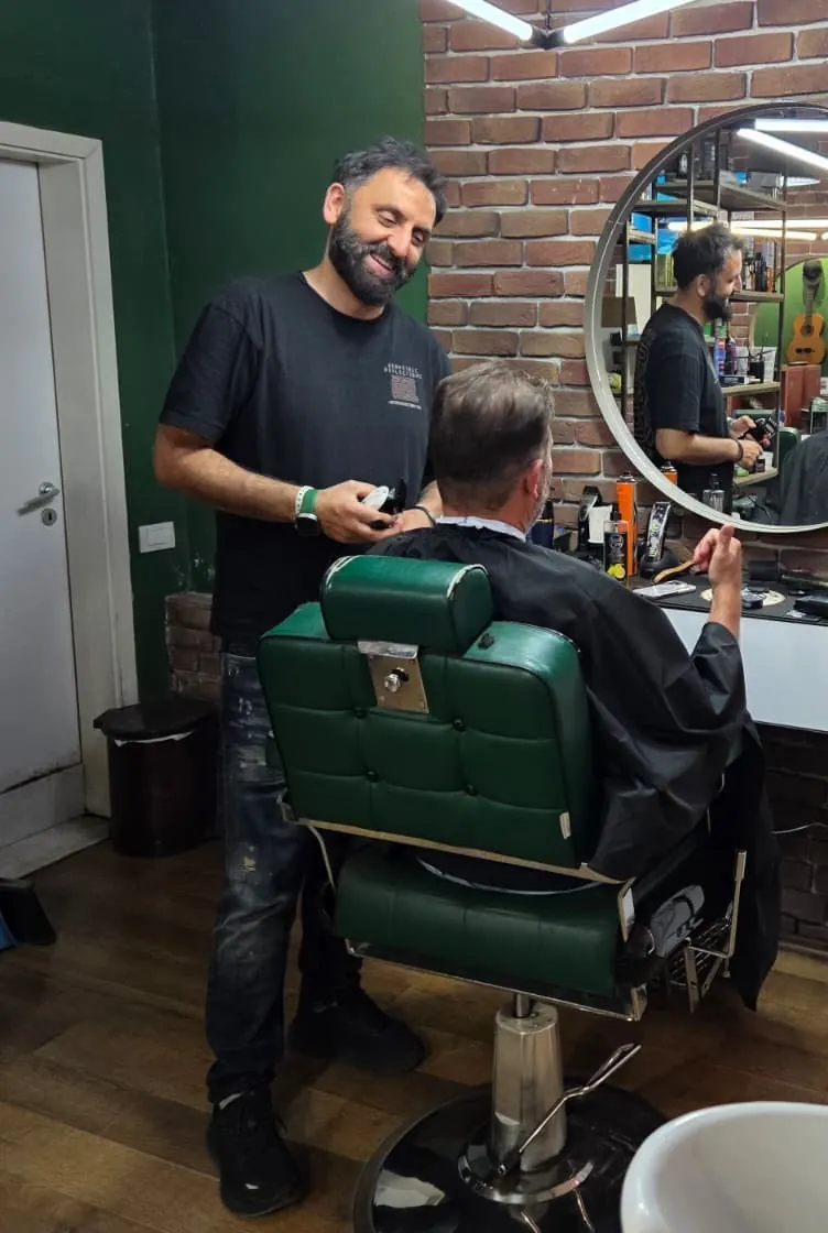 The barber at work behind a client in a green leather chair